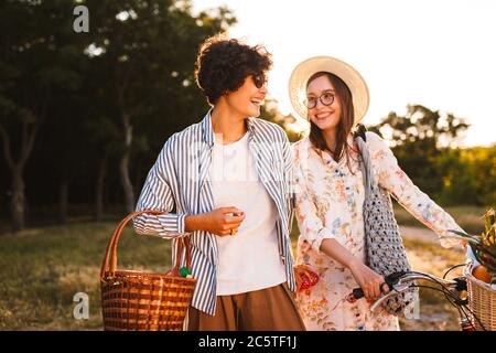 Zwei schöne lächelnde Mädchen mit Fahrrad und Korb glücklich schauen Stockfoto