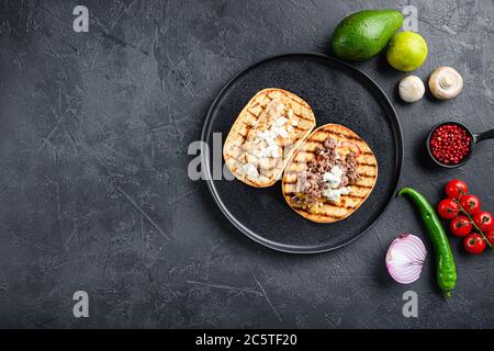 Mexikanische Tacos mit Gemüse und Bienenaf und Hühnerfleisch auf schwarzem runden Teller über texturiertem schwarzem Hintergrund, Draufsicht mit Platz für Text. Stockfoto