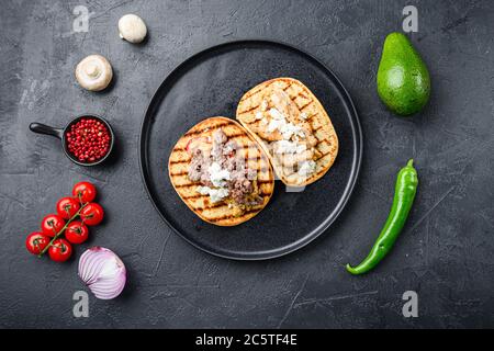 Traditionelle mexikanische Tortilla mit einer Mischung aus Zutaten eine Seite auf schwarzem Teller über schwarz texturierten Hintergrund Draufsicht. Stockfoto