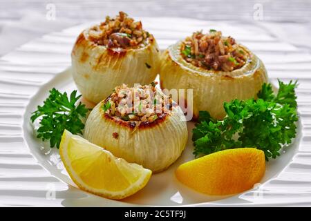 Nahaufnahme einer Portion karamellisierter gebratener ganzer Zwiebeln, gefüllt mit gehacktem Lamm und Reis auf einem Teller mit Zitronenkeilen, Landschaftsansicht Stockfoto