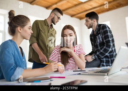 Zwei hübsche Mädchen arbeiten zusammen in modernen Büro mit Kollegen auf Hintergrund. Gruppe von kreativen Menschen, die Zeit bei der Arbeit verbringen Stockfoto