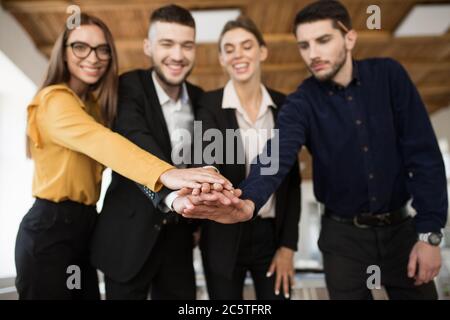 Gruppe lächelnder Geschäftspartner in Anzügen, die Einheit mit den Händen zeigen und gleichzeitig Zeit im modernen Büro verbringen Stockfoto