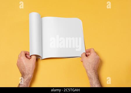 Männliche Hand öffnete einen Präsentationskatalog auf gelbem Hintergrund, editierbare Modell-up-Serie Vorlage bereit für Ihr Design, Auswahlpfad enthalten. Stockfoto