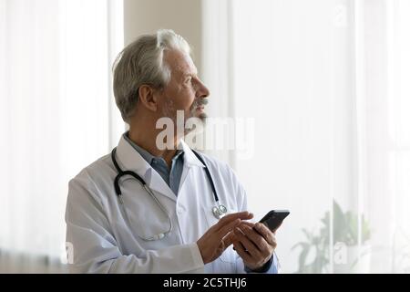 Pensive Senior männlich Arzt verwenden Handy denken Stockfoto