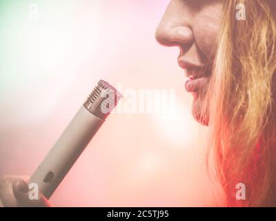 Ein Fragment eines weiblichen Profils, das ein altes sowjetisches Mikrofon am Mund hält. Foto mit einem rosa Filter Stockfoto