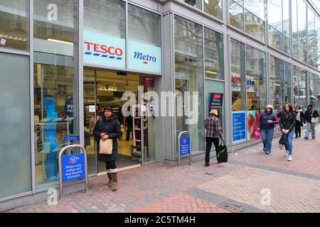 BIRMINGHAM, Großbritannien - 19. APRIL 2013: Menschen gehen durch Tesco Metro-Lebensmittelgeschäft in Birmingham, Großbritannien. Es gibt 3,400 Tesco-Läden in Großbritannien. Stockfoto