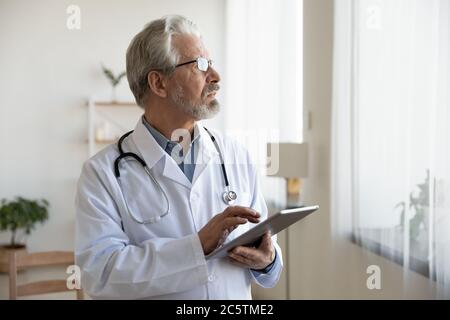 Pensive Senior Arzt verwenden Tablette Entscheidungsfindung Stockfoto