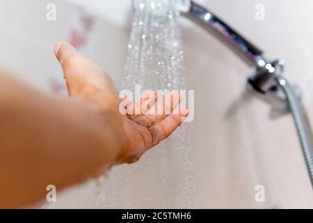 Männlich und unter dem Strom von Wasser aus der Dusche, überprüft die Wassertemperatur selektiven Fokus Stockfoto