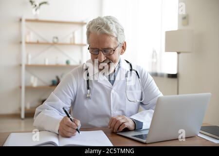 Lächelnder älterer männlicher Arzt schreiben in medizinische Zeitschrift Stockfoto