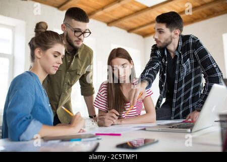 Gruppe von pensive Geschäftsleute und Frauen arbeiten mit Skizzen, während die Zeit bei der Arbeit. Junge Menschen überlegt, gemeinsam ein neues Projekt zu schaffen Stockfoto