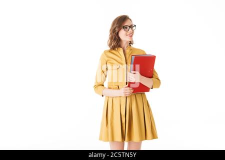Portrait von nett lächelnd Dame in Brillen und gelbes Kleid stehen mit roten Ordner in der Hand und Blick beiseite auf weißem Hintergrund isoliert Stockfoto