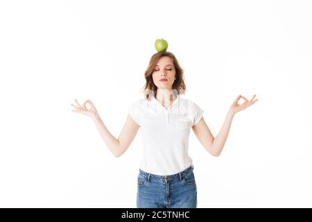 Portrait der jungen Dame stehen mit grünen Apfel auf dem Kopf und meditieren auf weißem Hintergrund isoliert Stockfoto