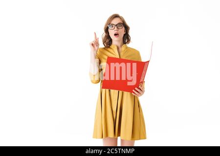 Portrait von hübschen Dame in Brillen und gelben Kleid hält roten Ordner, während erstaunt in der Kamera auf weißem Hintergrund isoliert Stockfoto