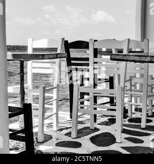 Tische und Stühle auf der Cafeterrasse am Meer, Mykonos, Griechenland. Schwarzweiß-Fotografie Stockfoto