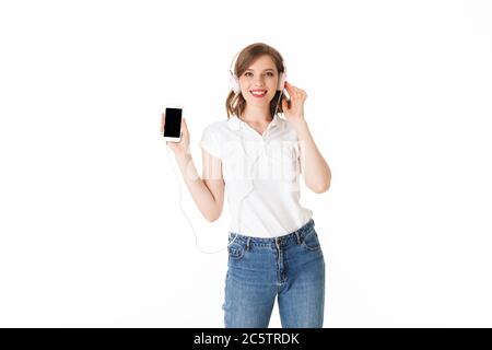 Portrait von ziemlich lächelnden Dame in Kopfhörer mit Handy in der Hand stehen und glücklich in der Kamera auf weißem Hintergrund isoliert suchen Stockfoto