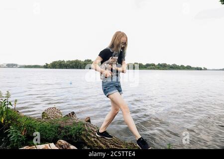 Eine junge Frau geht im Sommer mit einem drei Monate alten schottischen Reed Kätzchen in der Nähe des Sees. Das Foto wurde im Gesamtplan bei sonnigem Wetter mit natürlichem Licht aufgenommen Stockfoto