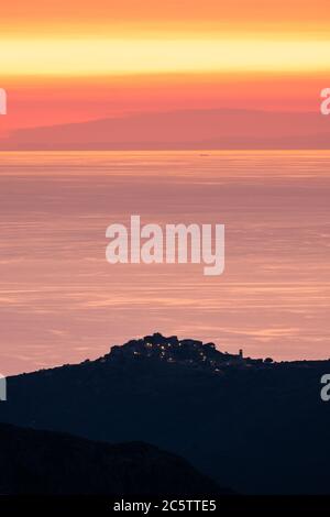 Sonnenuntergang über dem ruhigen Mittelmeer Meer mit der Silhouette des Hügeldorfes Sant'Antonino auf Korsika im Vordergrund und Küste von Frankreich in Stockfoto