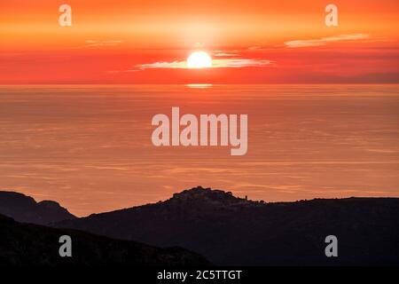 Sonnenuntergang über dem ruhigen Mittelmeer mit der Silhouette des Dorfes Sant'Antonino auf Korsika im Vordergrund und an der Küste von Franc Stockfoto