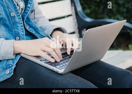 Kaukasischer Mann sitzt auf einer Bank und tippt auf einem Laptop. Stockfoto