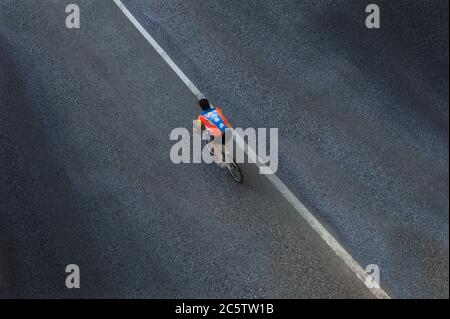 Einsam verschwommener Radfahrer oder Biker mit Hemd, aber ohne Helm auf einer Asphaltstraße mit nur einer weißen Linie, die diagonal im Foto ist. Blick von oben Stockfoto