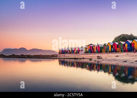 Blick auf den wunderschönen Sonnenuntergang über False Bay von Kalkbay mit kleinen farbigen Häusern am Strand, mit Bergen im Hintergrund, Kapstadt, Süden Stockfoto