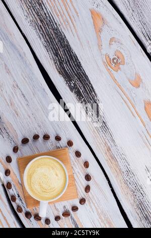 Tasse Kaffee mit Schaum, umgeben von Kaffeebohnen. Stockfoto