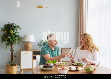 Portrait von liebevollen reifen Paar heben Champagner Glas und Toasten während genießen romantisches Abendessen zu Hause, kopieren Raum Stockfoto