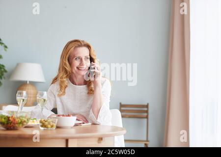 Portrait von eleganten reifen Frau sprechen per Telefon, während das Abendessen zu Hause genießen, kopieren Raum Stockfoto