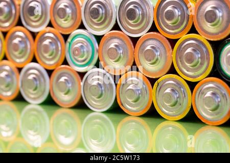 Mehrere verwendet AA Alkali-Mangan-Batterien werden gesehen in einem Stapel auf eine reflektierende grüne Oberfläche angeordnet. Closeup Vorderansicht aus der plus Seite der Batterie. Stockfoto