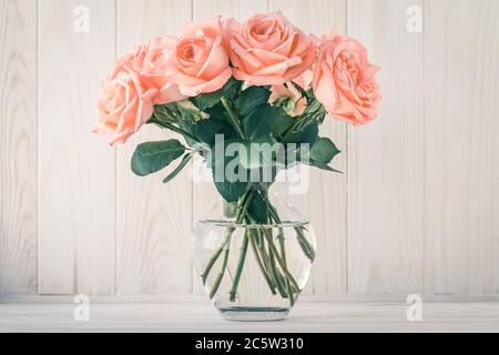 Blumenstrauß rosa Rosen in einer Vase auf einem Holzbrett Hintergrund. Stillleben im Retro-Stil. Vintage-Geschenkkarte, Feiertagskonzept Dekoration Stockfoto