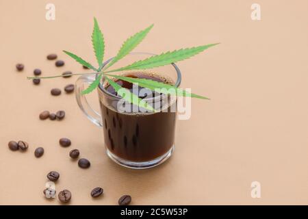 Tasse Kaffee mit Cannabisblatt und gerösteten Bohnen auf neutralem beigen Hintergrund mit Platz für Text Stockfoto