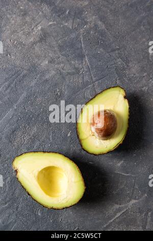Frische rohe Avocado-Hälften auf einem dunklen Steintisch, gesundes Esskonzept, Draufsicht mit Kopierraum Stockfoto