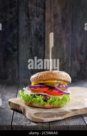 Köstlicher frischer hausgemachter Burger mit Käse, Tomaten, Salat, Gurken und Zwiebeln auf einem Holztisch, aus nächster Nähe Stockfoto