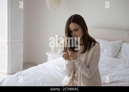 Unzufriedene unglückliche Frau, die auf dem Bett sitzt und die Haarspalten überprüft Stockfoto