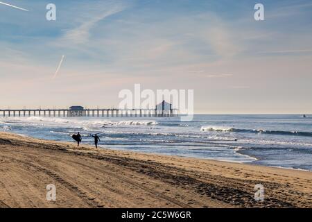 Die Wellenreiter laufen entlang des Huntington Beach in Kalifornien, mit dem Pier in der Ferne Stockfoto