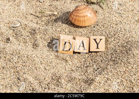 Tageswort aus Holzwürfeln. Nahaufnahme des Strandsands. Stockfoto