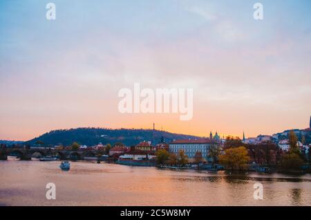 Dramatischer Sonnenuntergang in der Moldau mit einem vorbeifahrenden Boot und einem Gefälle von orangen bis rosa Farben, die sich vom Himmel ins Wasser spiegeln. Stockfoto