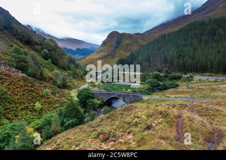 Thomas Telfords Steinbogenbrücke und die moderne A87 Hauptstraße überqueren den Fluss Shiel am EAS-nan-Arm in Glen Shiel unter den Bergen des Highla Stockfoto