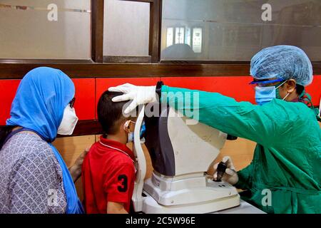 Ein Arzt, der eine persönliche Schutzausrüstung (PSA) trägt, um während des Coronavirus-Ausbruchs eine Augenuntersuchung eines Kindes in einer Augenklinik durchzuführen Stockfoto