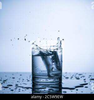 Wasser spritzt aus Eiswürfel im Glas Wasser, blauer Hintergrund Stockfoto