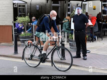 Ironbridge, Shropshire, Großbritannien, 5. Juli 2020. Seltsame Zeiten, wie Pubs, Restaurants und Geschäfte wieder öffnen ein Mitarbeiter im White Hart Pub trägt ein Gesichtsvisier, während er wartet, um Kunden zu begrüßen, während ein Radfahrer mit Gesichtsmaske vorbeikommt. Kredit: David Bagnall/Alamy Live Nachrichten Stockfoto