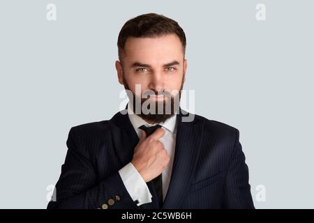 Schöner Herr im Geschäftsanzug, der seine Krawatte vor grauem Hintergrund anpasst Stockfoto