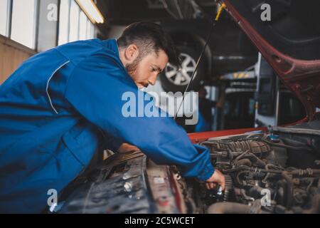 Männliche Auto Mechaniker in blauer Uniform repariert ein Auto Stockfoto