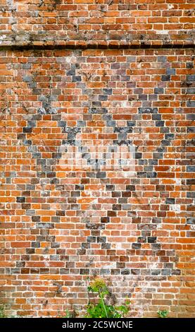 Zerbröckelnde Tudor gemusterte rote Ziegelmauerarbeiten mit einem dunkleren Ziegeldiamantmuster an einer Wand, Hampshire, England Stockfoto