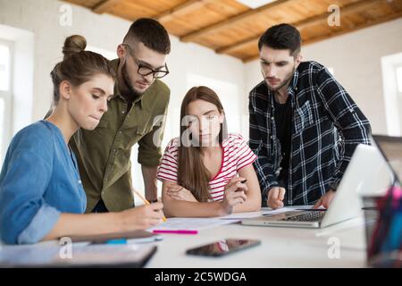 Gruppe von Geschäftsleuten und Männern, die mit Skizzen nachdenklich arbeiten, während sie Zeit bei der Arbeit verbringen. Junge Menschen schaffen gemeinsam ein neues Projekt in der Moderne Stockfoto