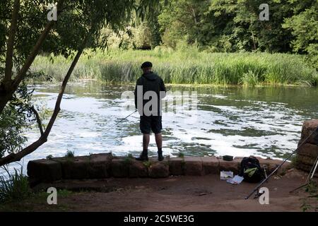 Ein Mann, der im Fluss Avon an der Saxon Mill, Warwick, Warwickshire, England, Großbritannien angeln kann Stockfoto