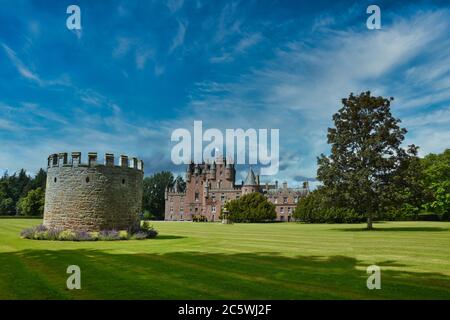 Glamis Castle in Schottland, mit großer Gartenanlage, Bäumen und runden Steingebäude an einem sonnigen Sommertag mit blauem Himmel und leichten Wolken Stockfoto