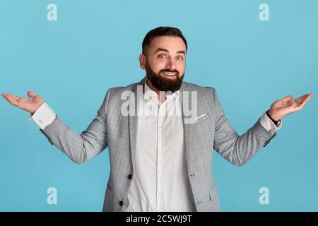 Unsichere tausendjährige Büroangestellte zucken auf blauem Hintergrund Stockfoto