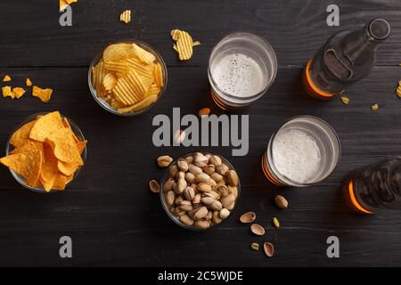Bier in Flaschen und Gläser, Chips, Nachos und Pistazien in Glasplatten und verstreut Stockfoto