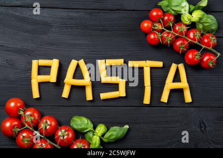 Wortpasta aus Tortiglioni Pasta Macaroni auf dem schwarzen Holztisch, reife Kirschtomaten und Basilikumblätter, Draufsicht Stockfoto